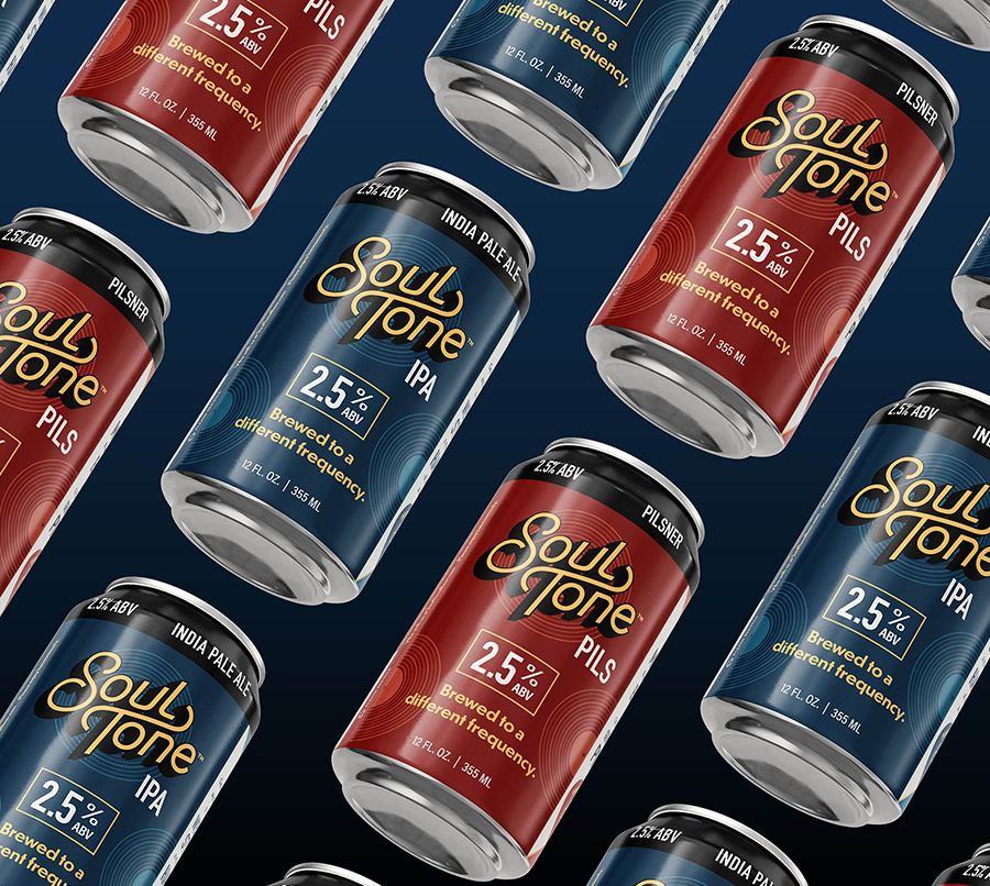 Cans of Soul Tone beer, including IPA in blue cans and Pilsner in red cans, are arranged in a diagonal pattern on a dark background. Each can displays 2.5% ABV and the phrase Brewed to a different frequency.